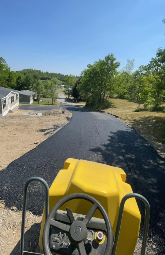 Yellow roller compacting new asphalt road through mobile home community