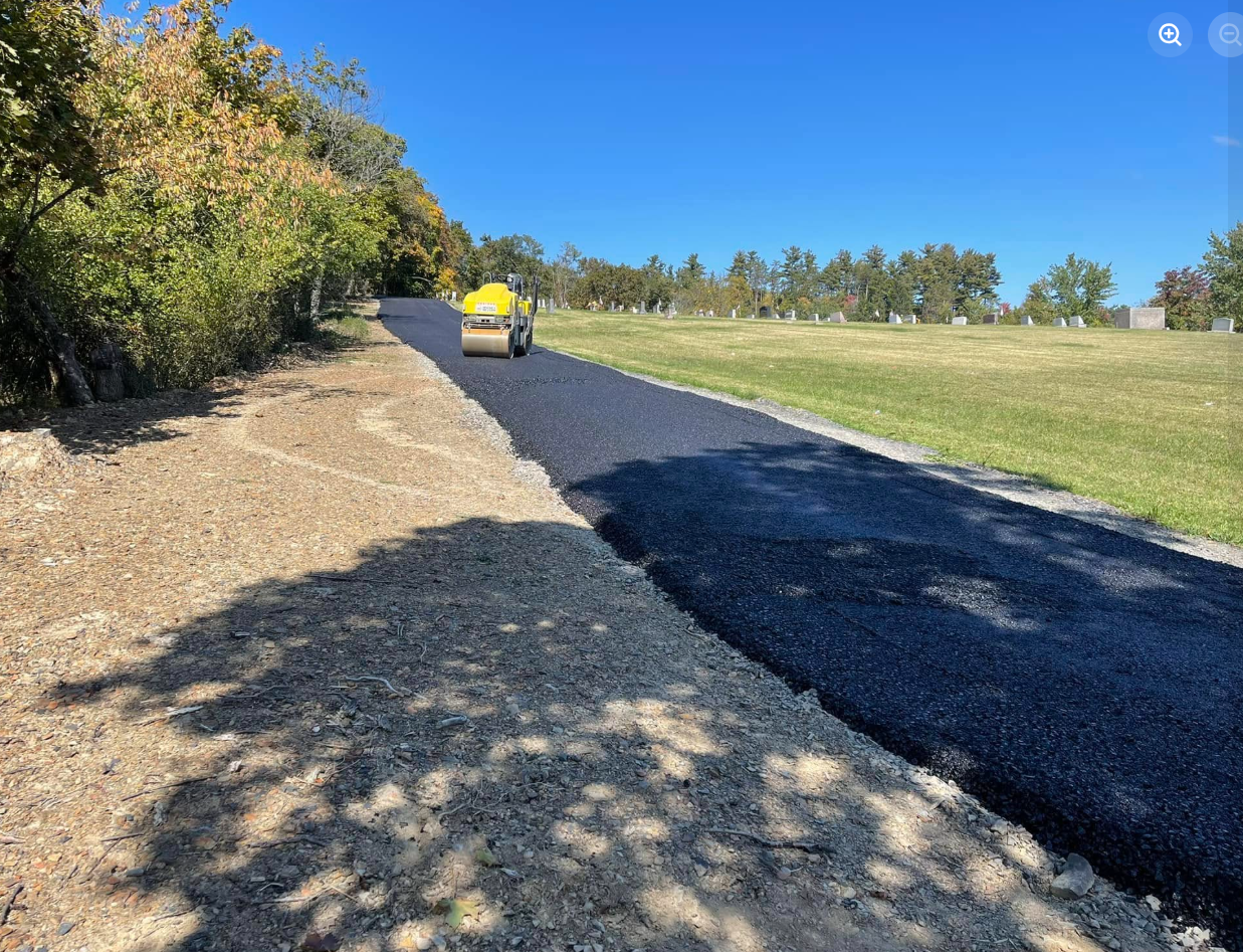 Yellow roller compacting fresh asphalt at cemetery road