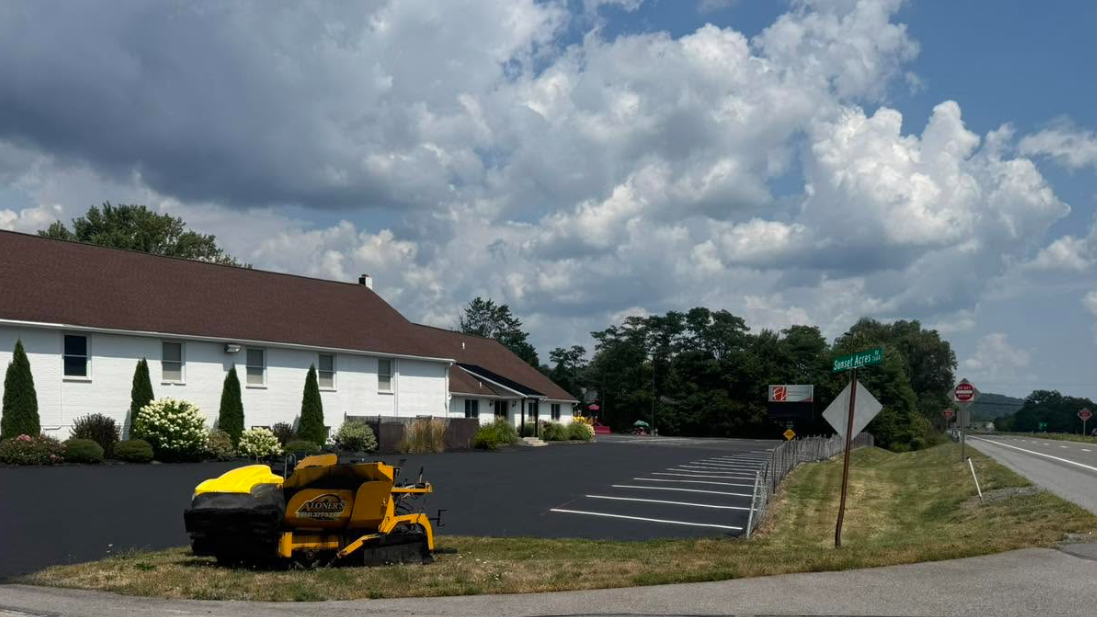 Aloners equipment sealcoating commercial parking lot at white building