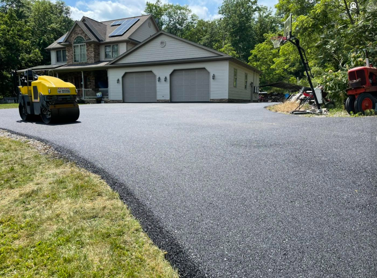Yellow roller compacting new asphalt at large residential home