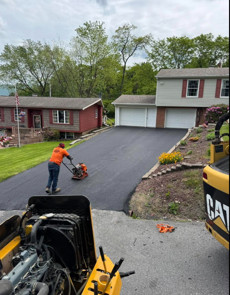 Crew compacting new asphalt driveway at brick suburban home