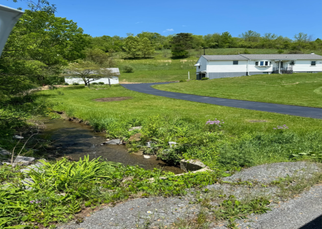 Newly paved curved driveway at rural white home with creek and green lawn
