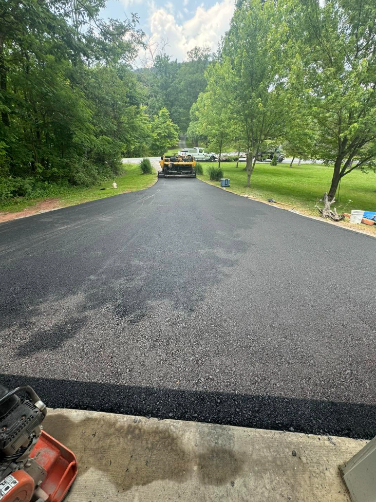 Yellow paver laying fresh asphalt on wide residential driveway in summer